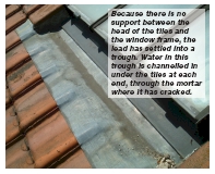 Because there is no support between the head of the tiles and the window frame, the lead has settled into a trough. Water in this trough is channelled in under the tiles at each end, through the mortar where it has cracked.